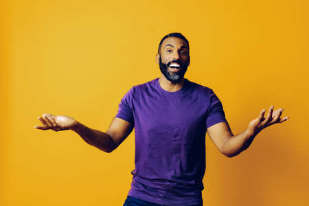 portrait of a successful winner man with a beard and a purple t-shirt celebrating with arm up on a yellow backgroundの写真素材