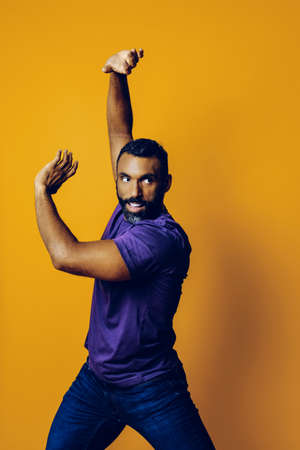 handsome man in a purple t-shirt with arms raised posing on a yellow background