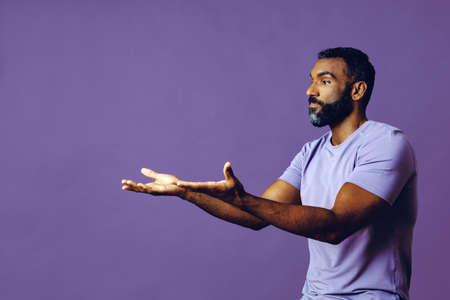 young black man with beard and mustache smiling and looking away at copy space hand signal isolated...