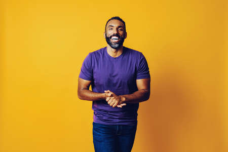 portrait of a successful smiling man with a beard and a purple t-shirt smiling with hands together on a yellow backgroundの写真素材
