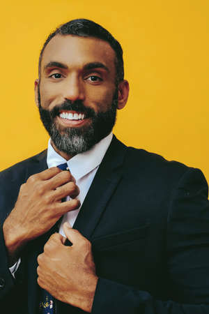 headshot of handsome positive smiling happy bearded man in suit with hand on tie, isolated on yellow backgroundの写真素材