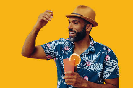 handsome bearded mid adult african american man wearing Hawaiian shirt and hat smiling with orange...