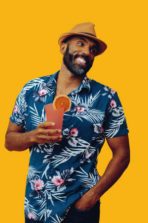 handsome bearded mid adult african american man wearing Hawaiian shirt and hat smiling with orange...