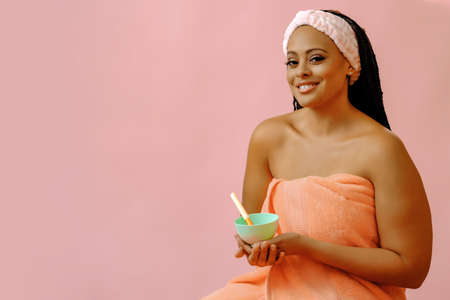 beauty black woman with perfect skin in towel clay body scrub application bowl looking at cameraの写真素材