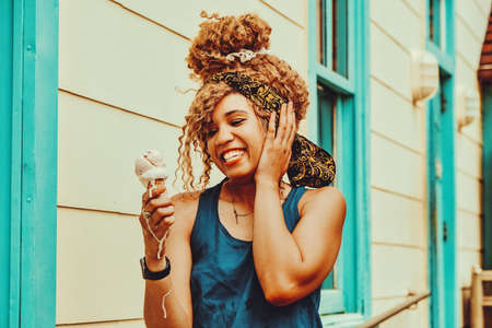 young adult woman afro hair smiling eating ice cream outdoors summertime looking awayの写真素材