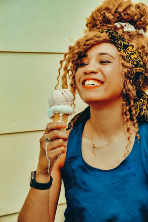 young adult woman afro hair smiling eating ice cream outdoors summertime looking awayの写真素材