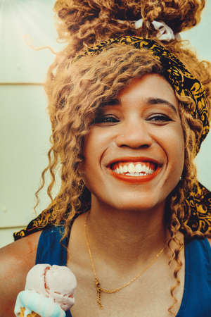 young adult woman afro hair smiling eating ice cream outdoors summertime looking at cameraの写真素材