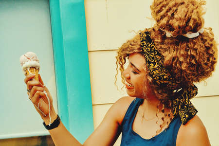 young adult woman afro hair smiling eating ice cream outdoors summertime looking awayの写真素材