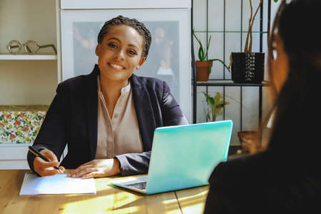 Young adult black executive businesswoman signing contract for client looking at camera in office