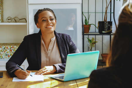 Young adult black executive businesswoman signing contract for client looking at client in officeの写真素材