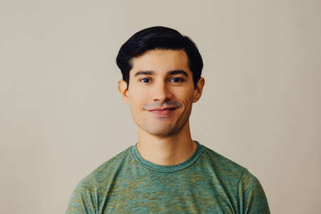 Headshot latino man black hair smiling handsome young adult green t-shirt over gray background...