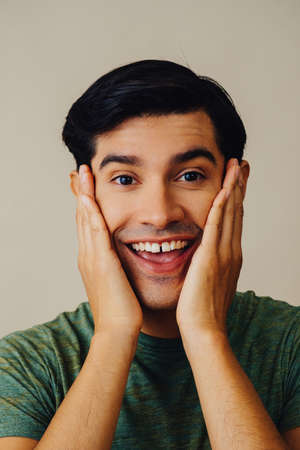 Headshot hispanic latino man smiling hands on cheek black hair hand covering mouth handsome young...