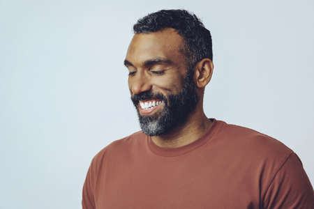 headshot portrait of a handsome bearded mid adult man smiling with eyes closed against gray...