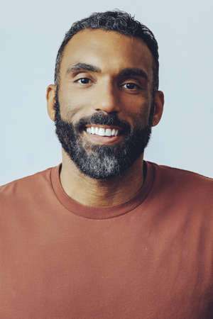 headshot portrait of a handsome bearded mid adult man looking at camera against gray background