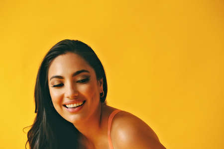 headshot beauty shot of hispanic Latina woman toothy smile young adult with black long hair and tank top in front of yellow background eyes closedの写真素材