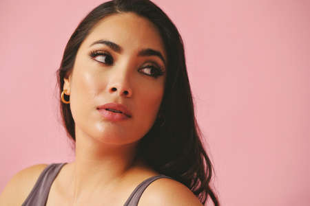 headshot of thoughtful hispanic Latina woman beauty young adult black long hair pattern pink dress in front of a pink background looking away at copy spaceの写真素材