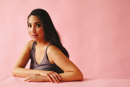 Portrait of thoughtful hispanic Latina woman beauty young adult black long hair pattern pink dress in front of a pink background looking at cameraの写真素材