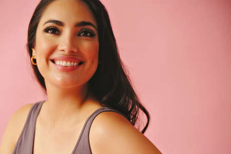 headshot of hispanic Latina woman smiling beauty young adult black long hair pattern pink dress in front of a pink background looking away at copy space studio shotの写真素材
