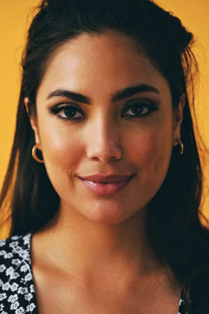 headshot beauty shot of sensual thoughtful hispanic Latina woman young adult with black long hair and dress in front of yellow background looking at cameraの写真素材