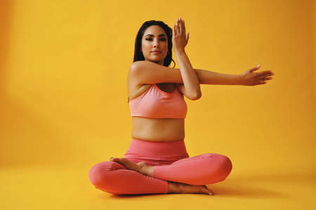 waist up portrait of hispanic beauty Latina woman stretching arms sports outfit young adult in front of yellow background looking at cameraの写真素材