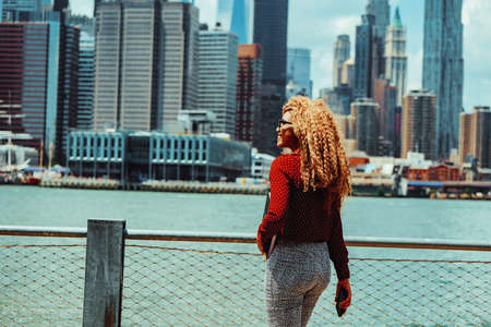 Portrait young adult entrepreneur millennial woman with eyeglasses and afro hair walking commuting with Manhattan New York City skyline skyscraper backgroundの写真素材