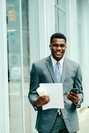 Positive young businessman using smartphone outside wearing suitの写真素材