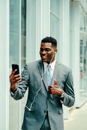 Positive young businessman using smartphone outside wearing suitの写真素材