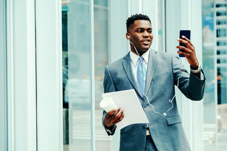 Positive young entrepreneur using smartphone outside wearing suitの写真素材