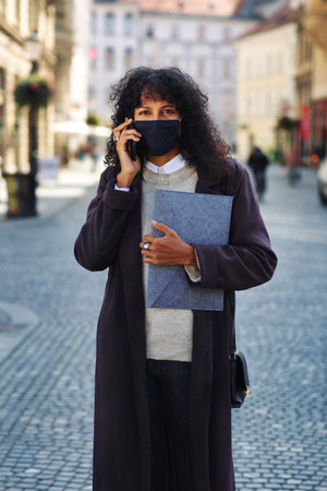 businesswoman outdoors with face mask talking on phoneの写真素材