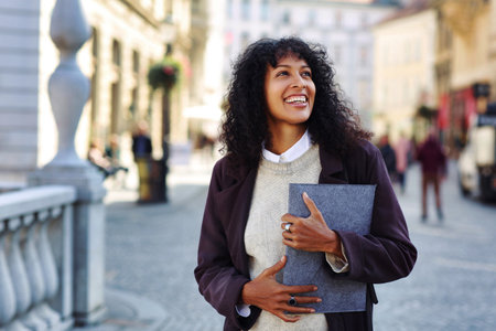 positive businesswoman standing on street holding folder with documentsの写真素材