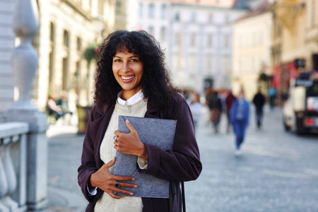 positive businesswoman standing on street holding folder with documentsの写真素材