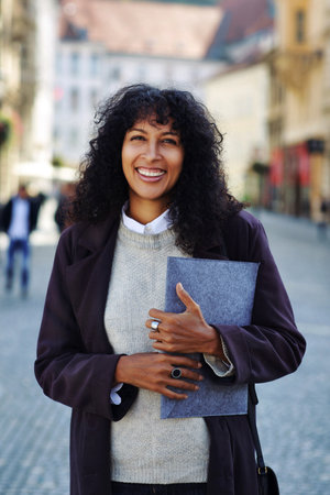 positive businesswoman standing on street holding folder with documentsの写真素材