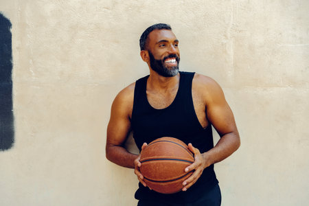 A bearded male athlete exercises indoors, dribbling a basketball. He wears a sleeveless tank top and looks determined in his pursuit of success.の写真素材