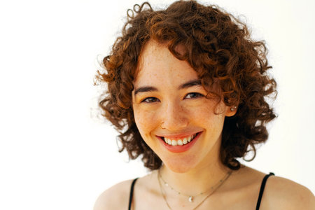 closeup, young adult woman with curly hair smiling, looking at cameraの写真素材
