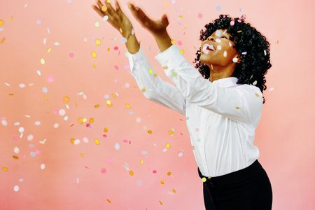 A special occasion - Portrait of a happy woman with arms out, smiling at confetti falling. Studio shot over pink backgroundの写真素材
