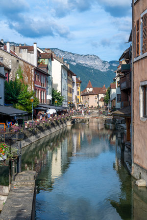 A city street with a canal running through it. The canal is filled with water and has a reflection of the buildings on the water. The street is lined with shops and restaurants. Annecy, Franceの写真素材