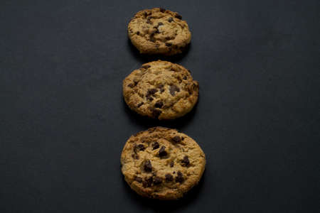 Three chocolate chip cookies in vertical line on black background.の写真素材