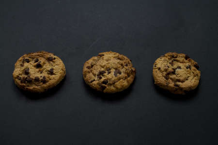 Three chocolate chip cookies in horizontal line on black background.の写真素材