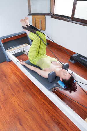 20 to 30 latin woman in pilates reformer machine workout wearing green clothes. High quality photoの写真素材