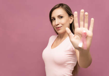 woman shows the ribbon symbolizing the fight against breast cancer wearing a pink t-shirt and posing in front of a wall. High quality photoの写真素材