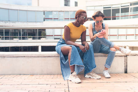a couple of young stylish women smiling and watching smartphone outdoor. High quality photoの写真素材