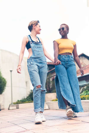 a couple of young women walk down the street holding hands during a sunny day. High quality photoの写真素材