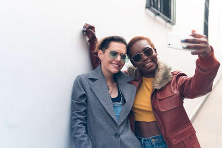 young couple of beautiful and multiethnic women taking a selfie looking happy in the street. High quality photoの写真素材