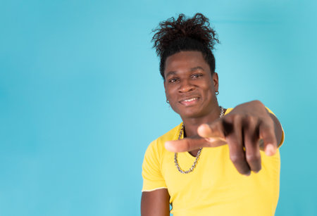 young latin afro man pointing to the camera in front of a blue background in a studio shot. High...