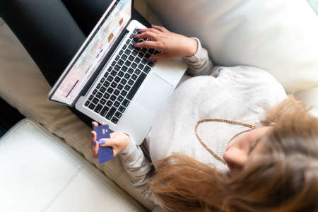 young woman sitting on the sofa shopping online with a credit card on her hand. High quality photoの写真素材