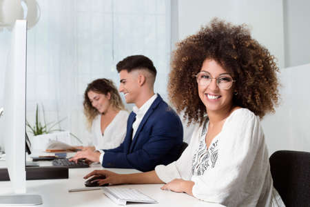 some young coworkers working in the office. There are two women and a man.They look like happy. They...