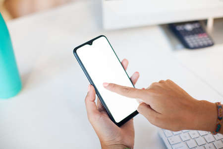 Close up woman hand using a smart phone with blank screen at office over workplace