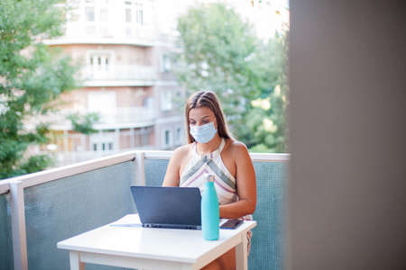 Head shot young woman wearing protective mask working from home office due to coronavirus outbreakの写真素材