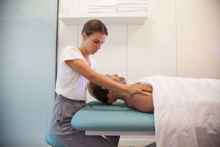 Female physiotherapist giving head massage to male patient