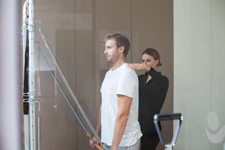 young man doing pilates exercise on reformer with his female instructor